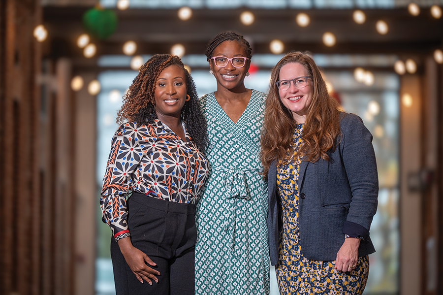 Three women stand in a long hallway.