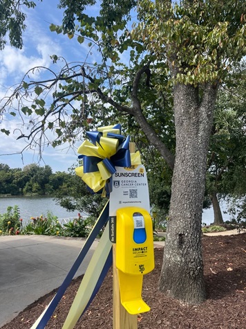 A Sunscreen dispenser outside from Impact Melanoma with the words "Impact Melanoma" underneath