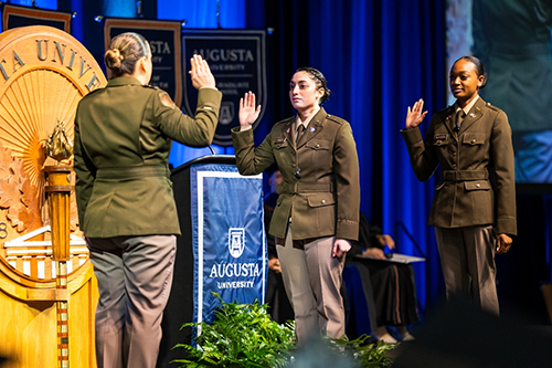Three females standing with their right arm raised.