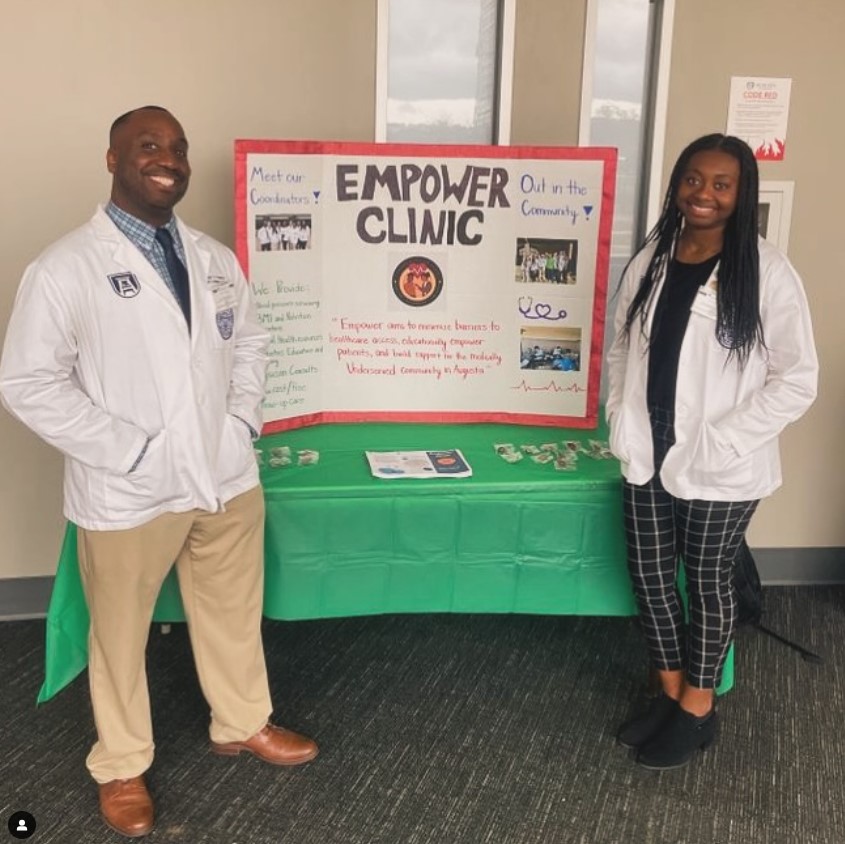 Two smiling students standing in front of a poster