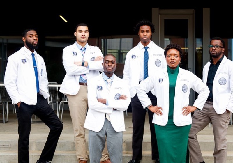 photo of a group of students in white coats on steps in front of building