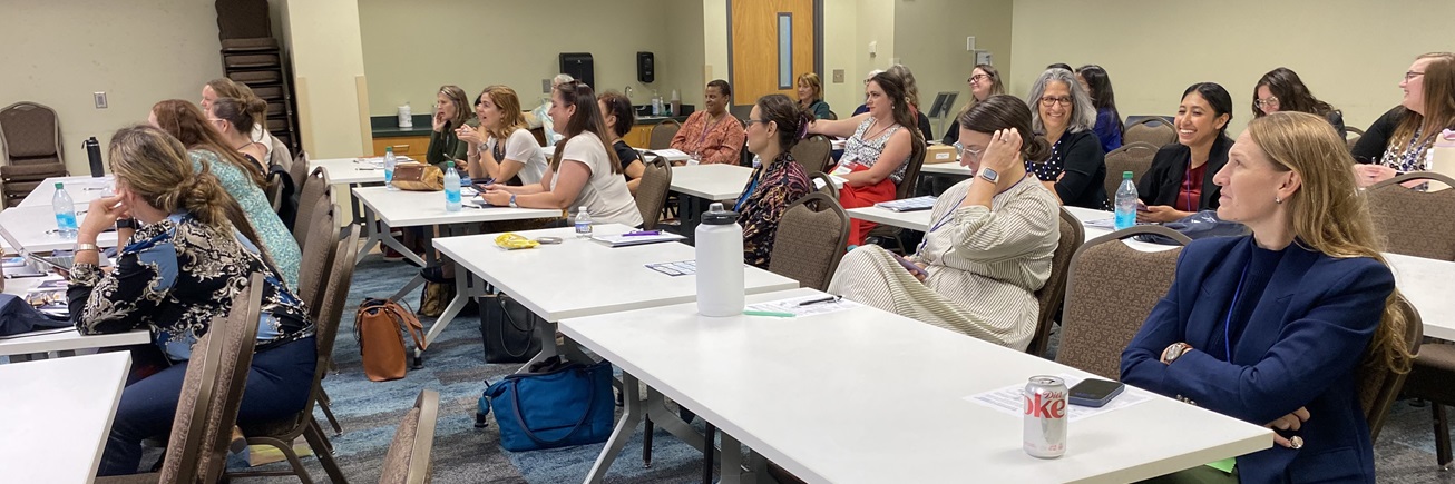 2025 Women's retreat photo of women sitting and smiling listening to a speaker