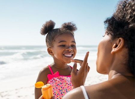 Mother applying sunscreen to daughter's face at the beach