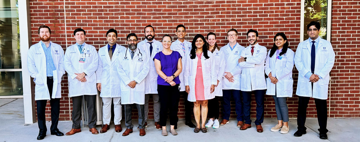 Group of 13 Hemoc Fellowship individuals pose for a picture outside the Georgia Cancer Center Outpatient Services sign in front of the building.