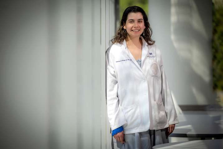 student standing in front of window in white coar