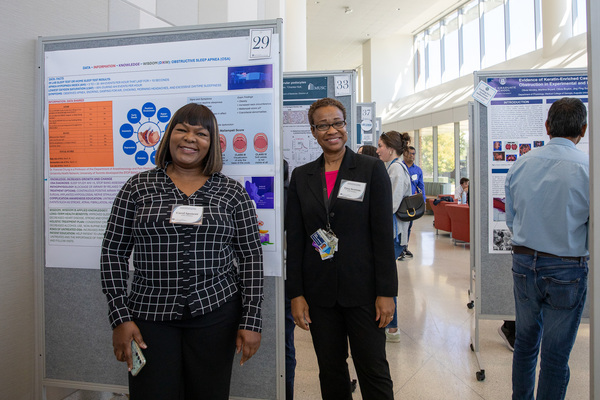 Two individuals smile in front of a poster at the Poster Presentations