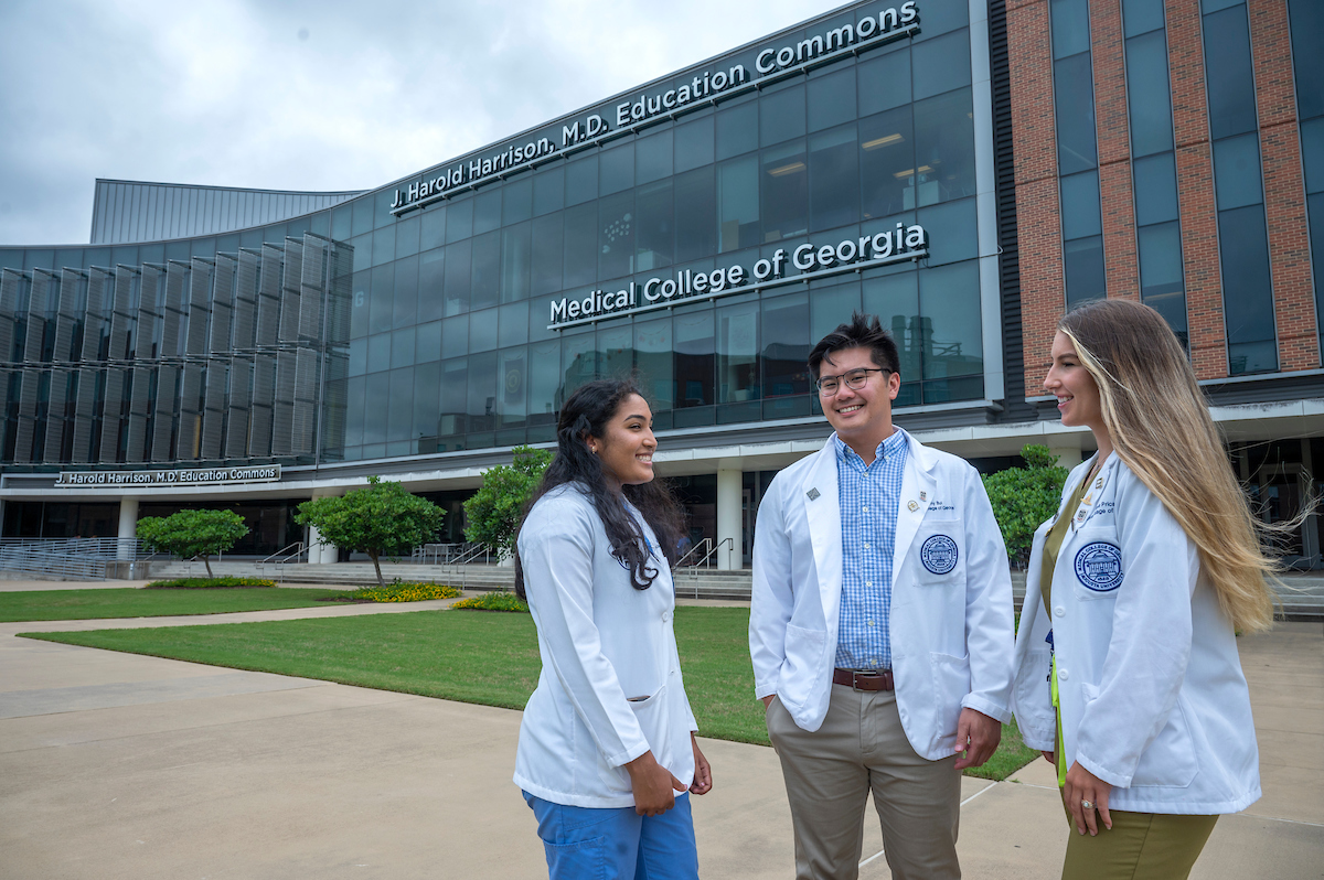 three students stand in front of building