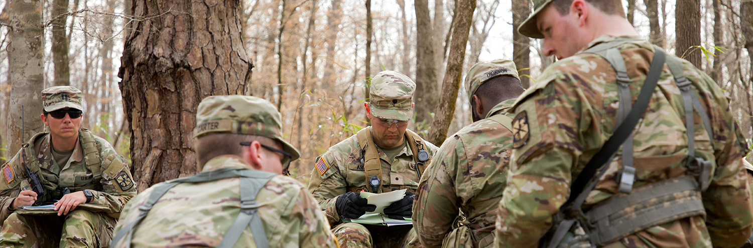 Cadets kneel in the woods as they plan for a mission