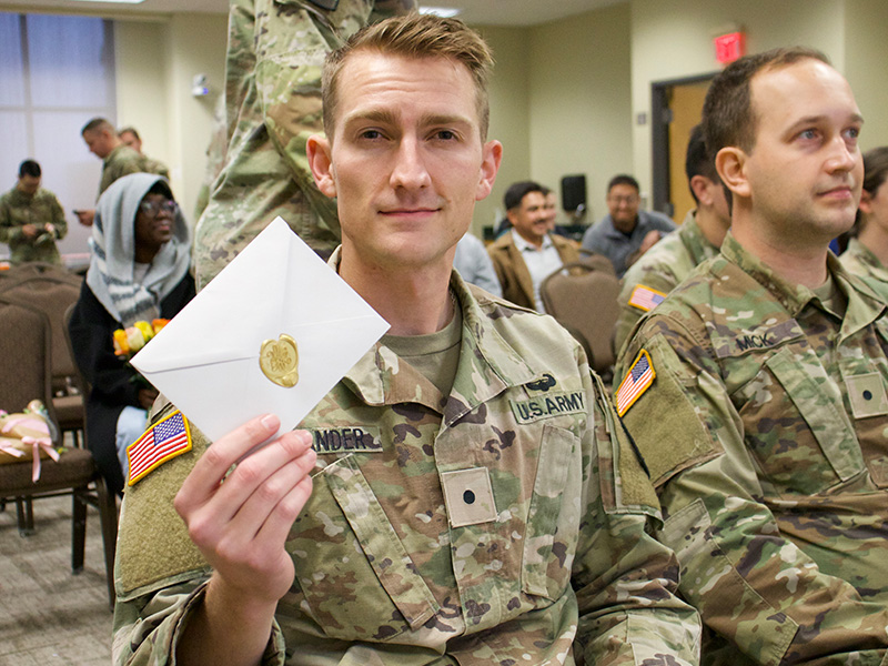 Cadet holds up a wax-sealed envelope to the camera