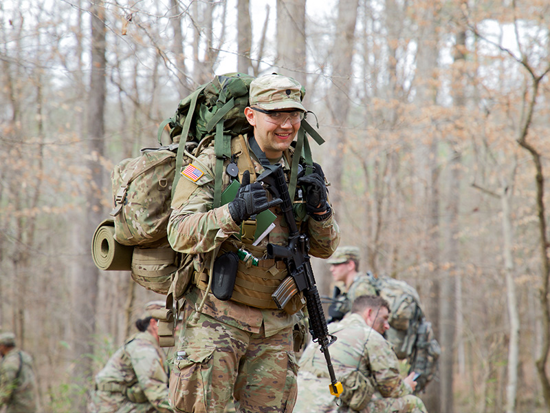 Cadet smiles for picture with gear on back, in the woods