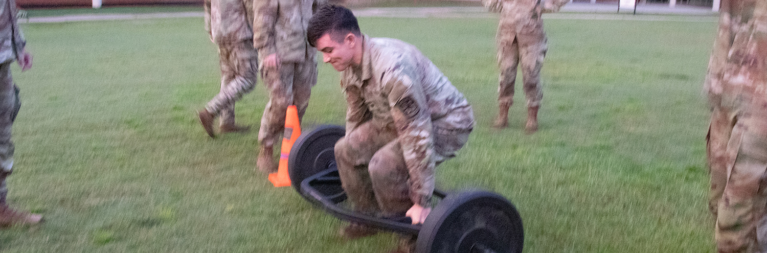 Cadet lifts deadlift bar off patch of grass