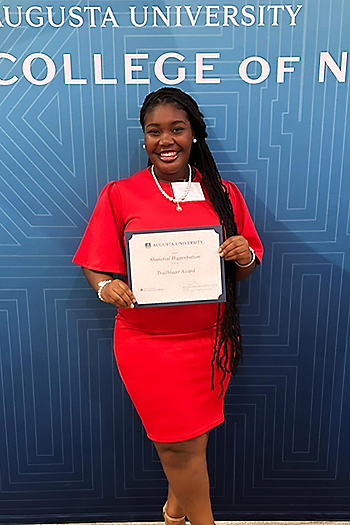 Picture of Shanerial Higgenbottom holding a scholarship in front of a blue background