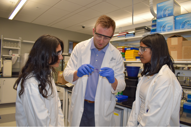 man and two women in lab coats looking at a slide