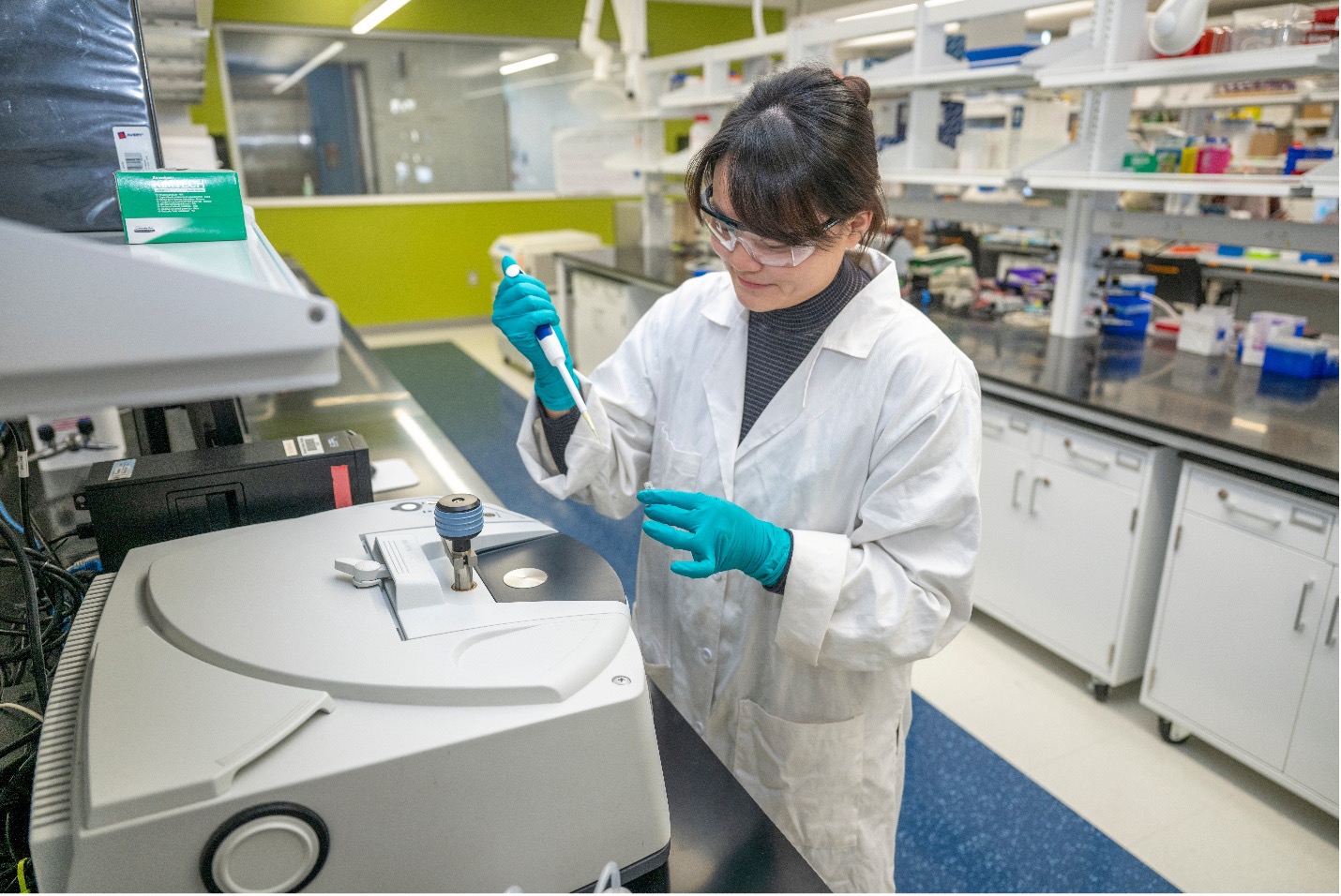 Dr. Chen Lab Photo A woman in a white lab coat and safety glasses, Dr. Xiaobing Chen, pipettes in her lab.