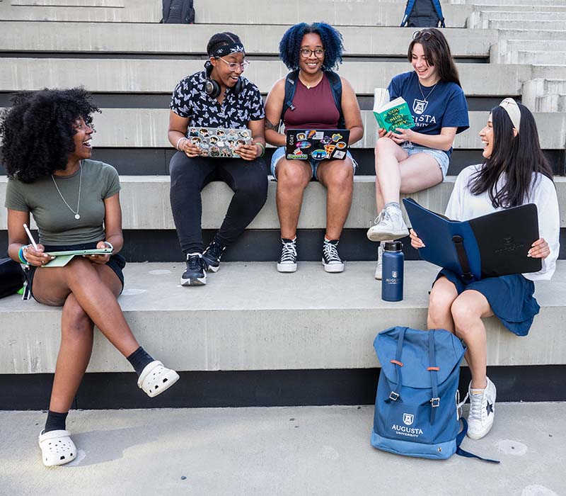 female students sitting on steps with lapstops talking and laughing with each other